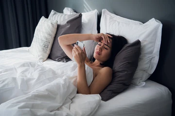 mulher triste com celular na cama