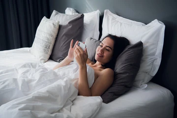 mulher lendo mensagens de texto na cama