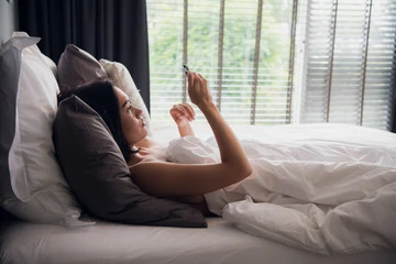 mulher lendo mensagens no celular na cama